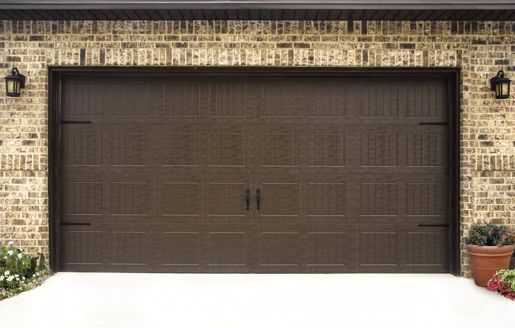 A traditional brown garage door with decorative hardware installed on a brick residential house by Overhead Doors Unlimited, LLC in Appleton, WI.