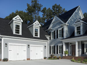 Two traditional white carriage-style garage doors with decorative hardware on a gray house by American Overhead Door in Madison, AL