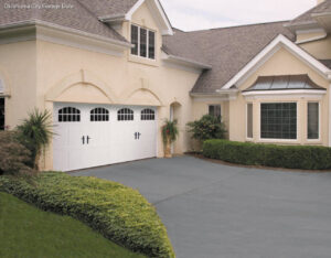 A traditional white garage door with arched windows on a stucco home, installed by CCM Overhead Doors in Oklahoma City, OK.