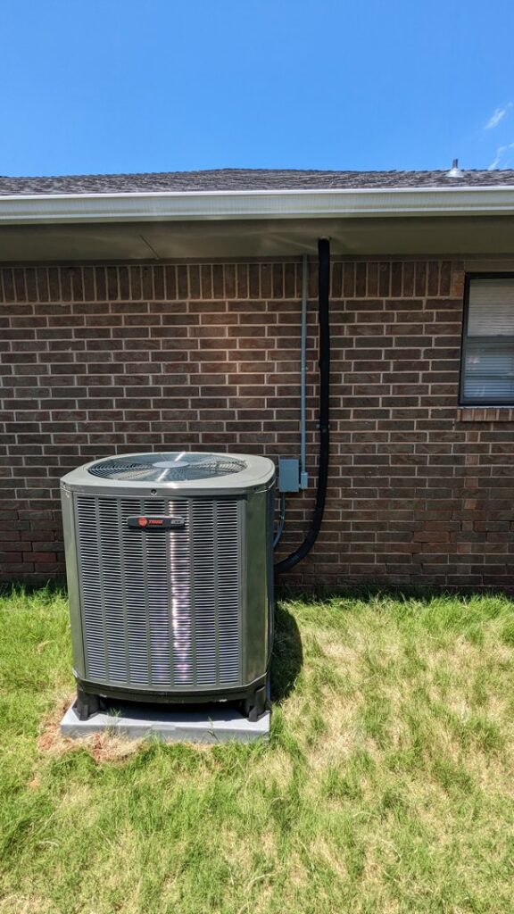 An outdoor Trane air conditioning unit installed next to a brick house by Totality Heating And Cooling in Edmond, OK.