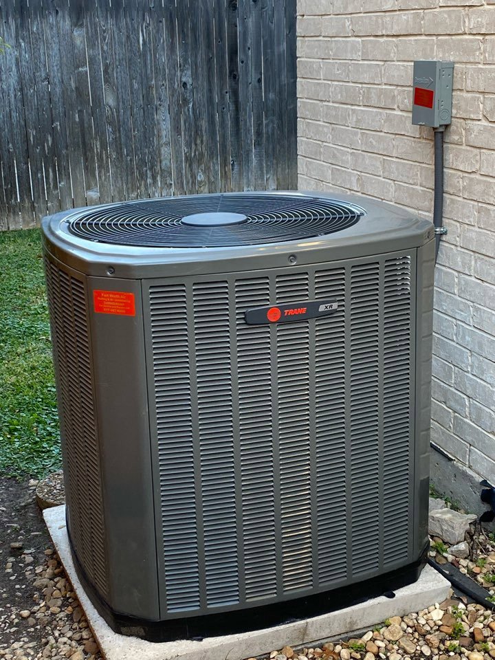 A Trane outdoor AC unit installed next to a brick wall and wooden fence by Fort Worth Air Conditioning Co. Inc. in Fort Worth, TX.