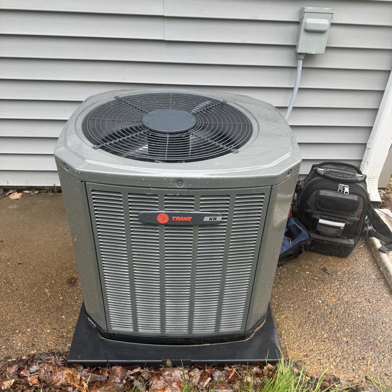 An outdoor Trane XR AC condenser unit with a technician's tool bag nearby, serviced by Hodges Heating & Cooling in Owensboro, KY.
