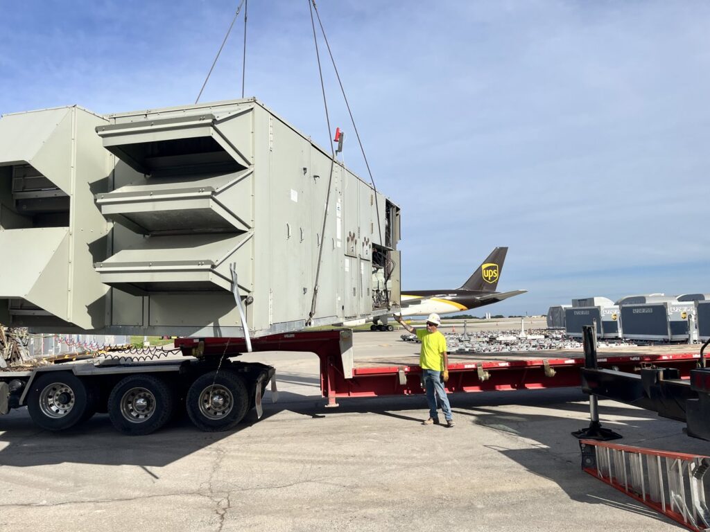 A large commercial HVAC unit on a flatbed trailer being transported for installation by DMC Service, Inc. in Olathe, KS.