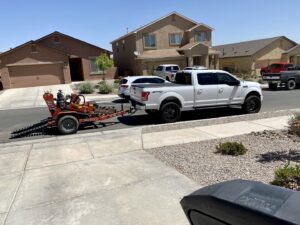 A white pickup truck towing trenching equipment, used for installing underground electrical or data lines by CAAM Integration LLC in Albuquerque, NM.