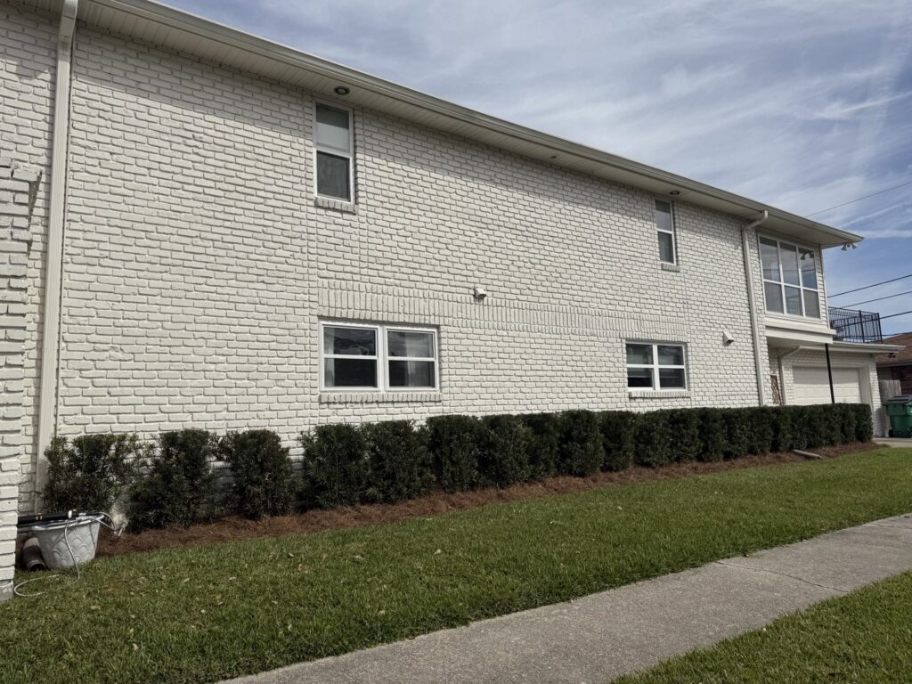 A long row of neatly trimmed hedges with fresh pine straw mulch along a white brick building by God's Sight Lawn & Gardens LLC in New Orleans, LA