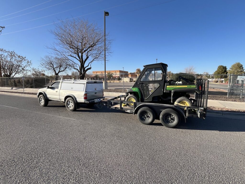 An El Valle Pest Control truck towing a utility vehicle on a trailer, used for pest and weed control services in El Paso, TX