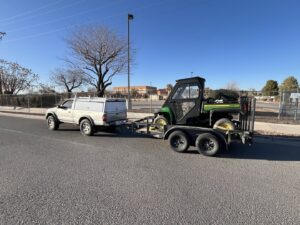 An El Valle Pest Control truck towing a utility vehicle on a trailer, used for pest and weed control services in El Paso, TX