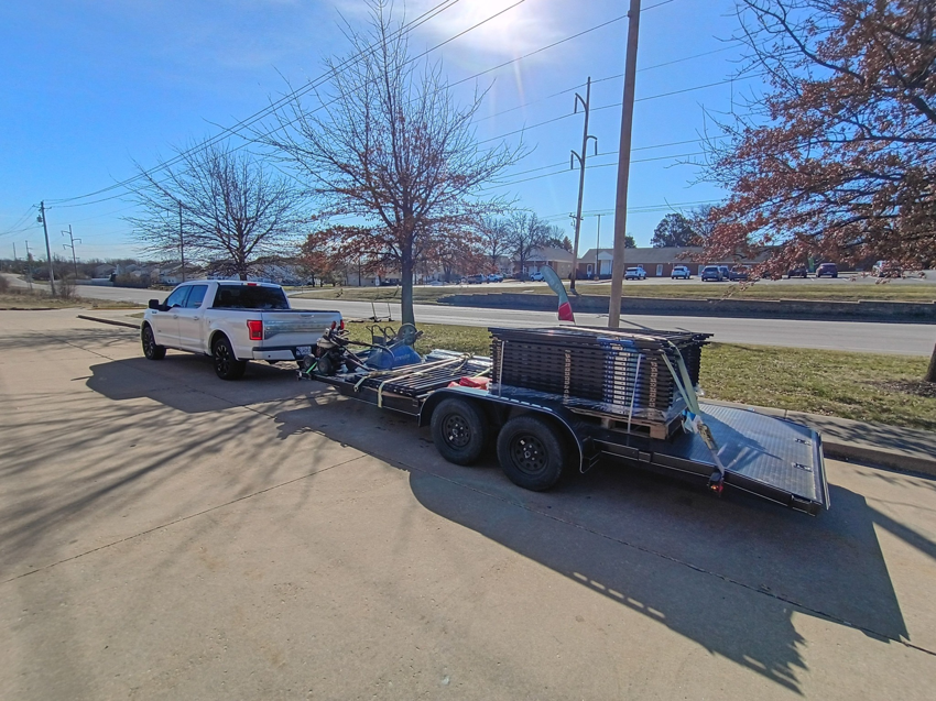 A white pickup truck towing a trailer loaded with fencing materials for Fence Experts STL in Fenton, MO