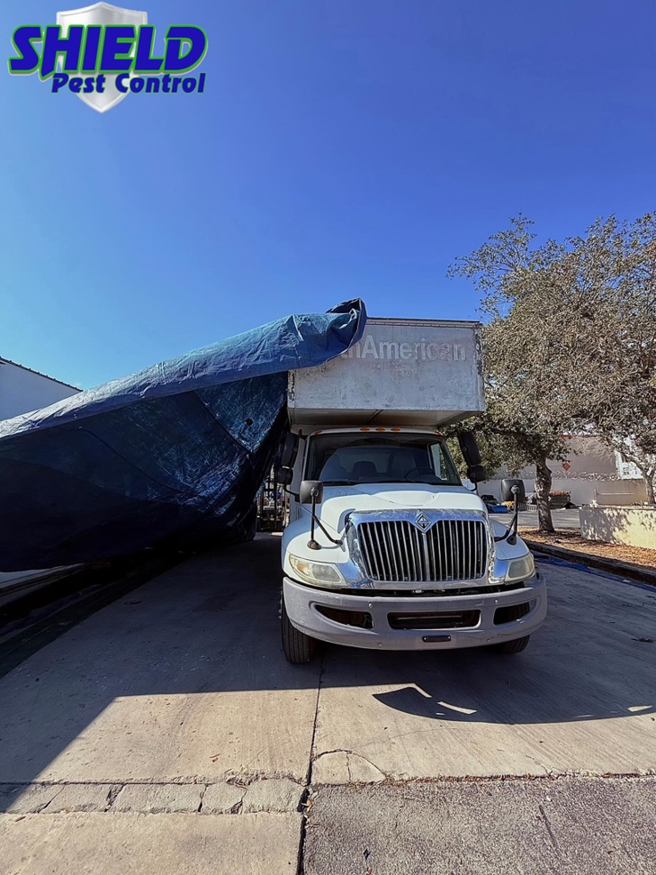 A Shield Pest Control truck with a large blue fumigation tarp, ready for a pest control job in Homestead, FL.