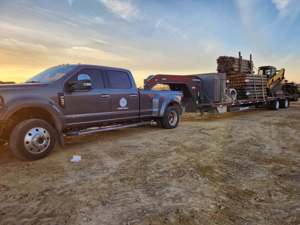 A work truck with a trailer loaded with fence posts and an excavator, ready for a job by H&S Fencing & Supply in Linden, WI.