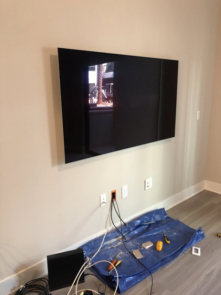 A wall-mounted TV with visible wiring and power outlets below, installed by PTech Installs in Columbus, GA.