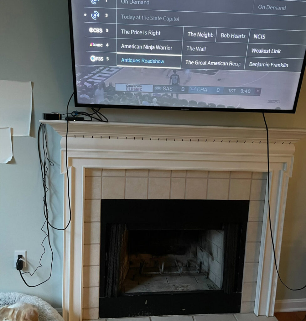 Wall-mounted television above a fireplace with electrical wiring and an outlet, showcasing services by Golden Electric in Danbury, CT.