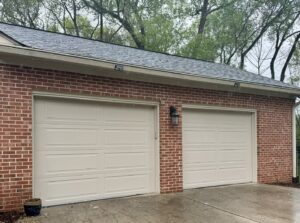 Two newly installed beige garage doors on a brick house by Precision Door Service of Huntsville, AL.