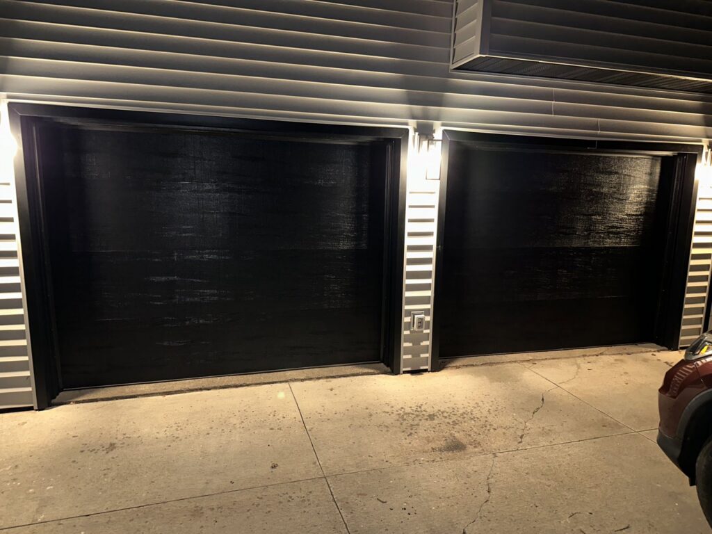 Two modern black garage doors on the exterior of a home at night by AJK Door Services in Duluth, MN.