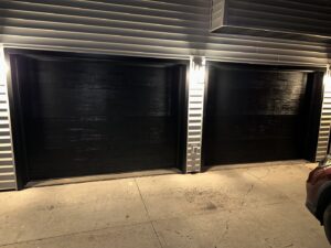 Two modern black garage doors on the exterior of a home at night by AJK Door Services in Duluth, MN.