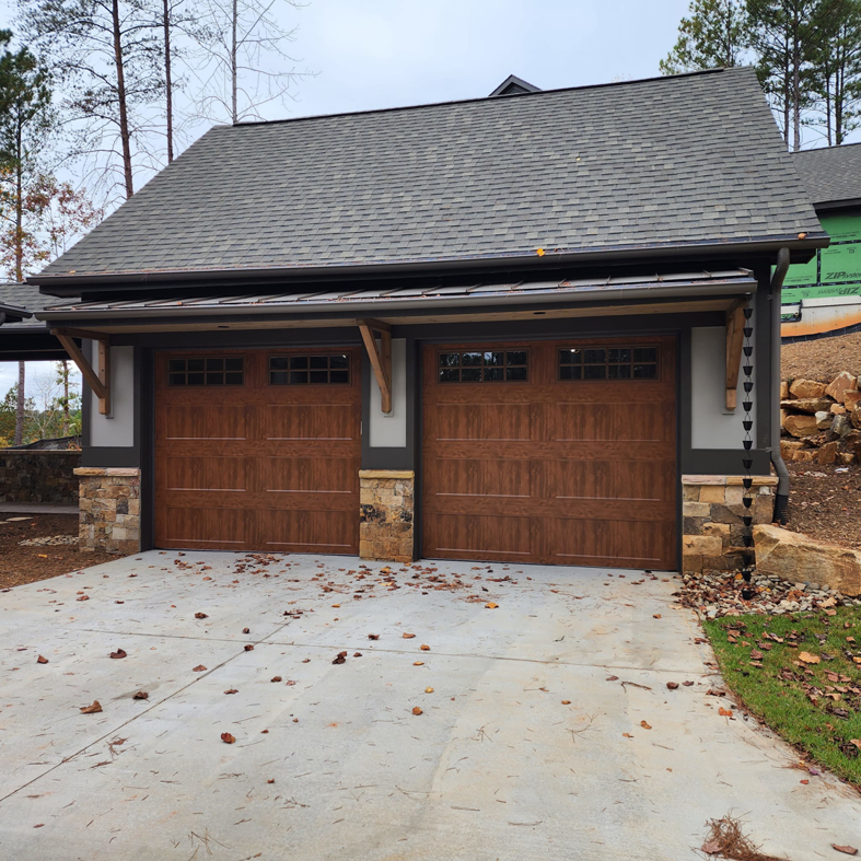Two brown carriage-style garage doors with windows installed on a home by Getsinger's Overhead Doors in Spartanburg, SC.