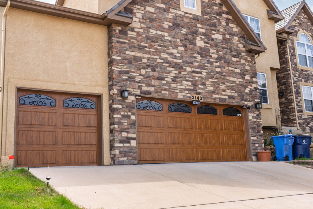 Two matching brown garage doors with decorative windows on a stone and stucco house by Prutch's Garage Door in Colorado Springs, CO