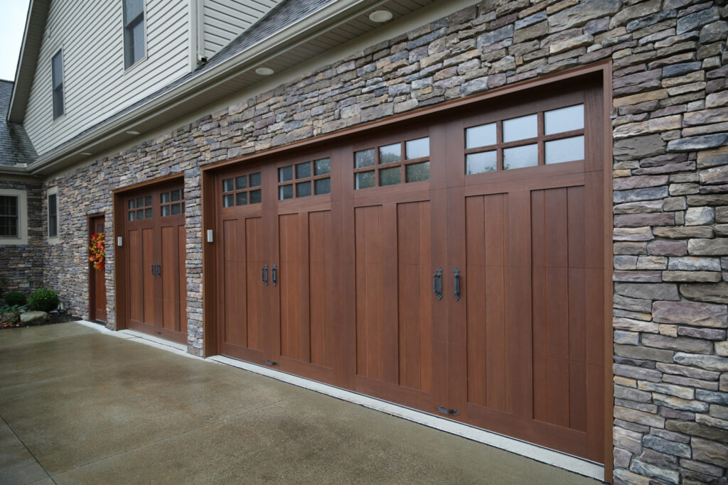 Two stylish brown garage doors with multiple windows on a stone house, a service from Madison Overhead Garage Door Services in Madison, WI.
