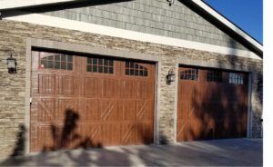 Two brown garage doors with arched windows on a stone and siding house by SCI Door in Yakima, WA
