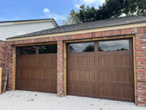 Two modern brown garage doors with windows on a brick garage by Tulsa Garage Door Doctor LLC in Tulsa, OK