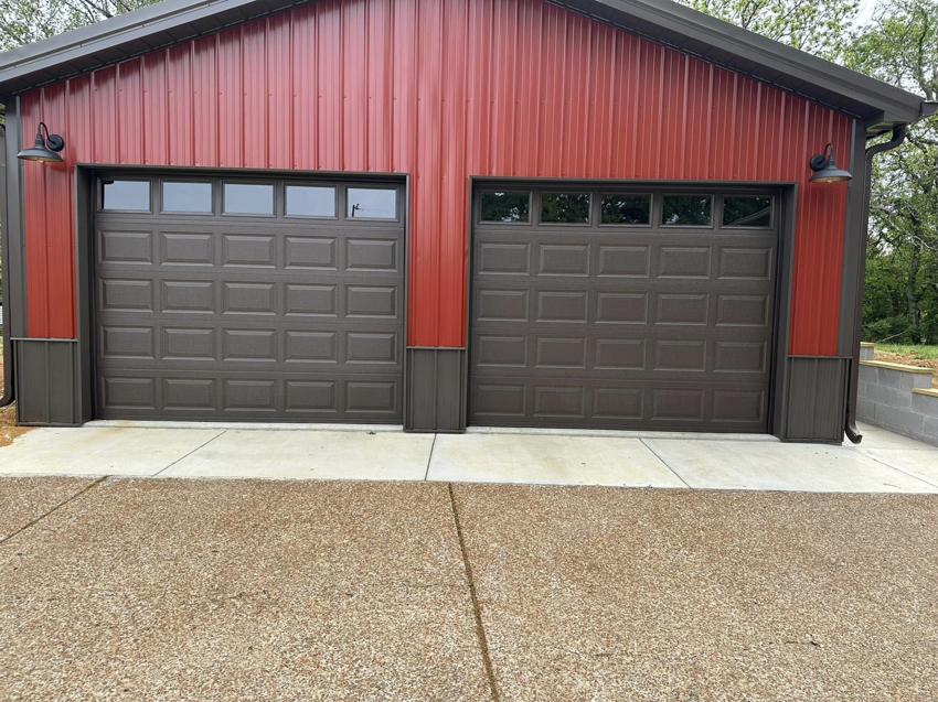 Two brown panel garage doors with windows installed on a red metal building by Up Garage Door in Nashville, TN.