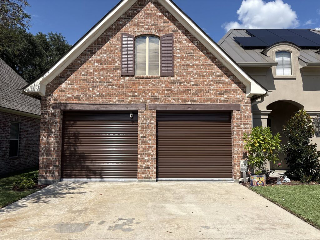 Two newly installed brown roll-up garage doors on a brick residential home by Superior Garage Door & Repairs in Lafayette, LA.