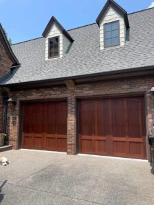 Two brown wooden-style garage doors installed on a brick house by Skylift Garage Doors - Knoxville, TN