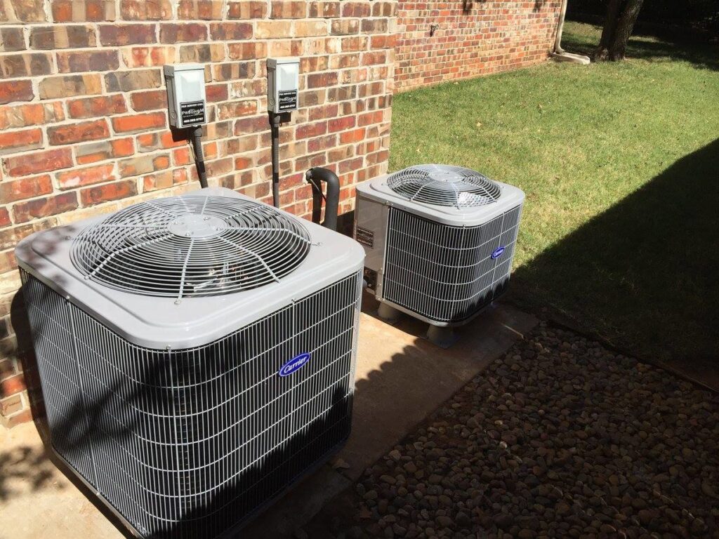 Two Carrier HVAC condenser units installed next to a brick building by Prudhom Mechanical LLC in Edmond, OK