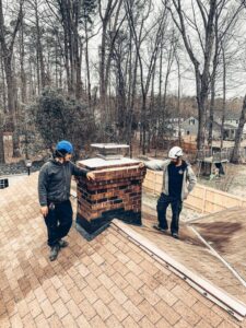 Two chimney sweep technicians working on a chimney on a roof for Rooftop Chimney Sweeps in Alexandria, VA.