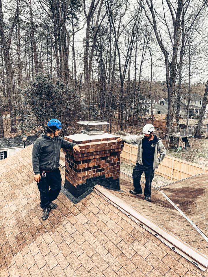 Two chimney sweep technicians working on a chimney on a roof for Rooftop Chimney Sweeps in Alexandria, VA.