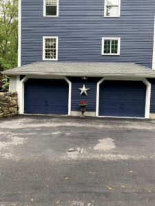 Two dark blue garage doors installed on a blue house by Snowbird Garage Doors Company in Worcester, MA.
