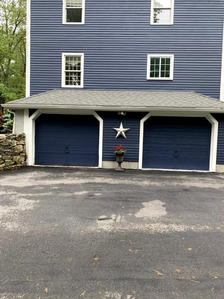 Two dark blue garage doors installed on a blue house by Snowbird Garage Doors Company in Worcester, MA.