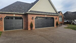 Two dark brown garage doors with decorative windows on a brick home, installed by A+ Garage Door Repair in Evansville, IN.