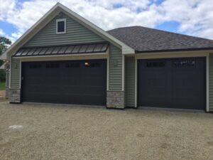 Two dark gray residential garage doors installed on a light green house by Tri County Overhead Door Service Inc in New London, WI