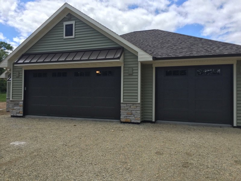 Two dark gray residential garage doors installed on a light green house by Tri County Overhead Door Service Inc in New London, WI