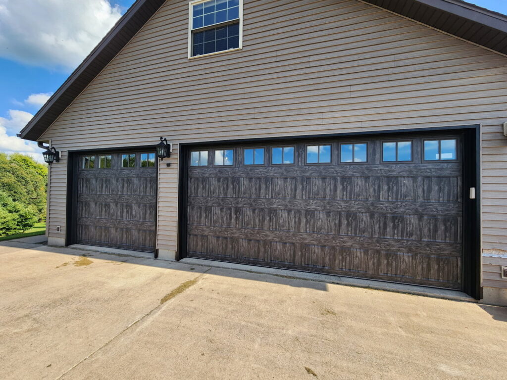 Two dark grey wood-grain garage doors with windows installed on a house by LabraDoor Overhead Services in Eau Claire, WI.