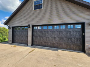 Two dark grey wood-grain garage doors with windows installed on a house by LabraDoor Overhead Services in Eau Claire, WI.