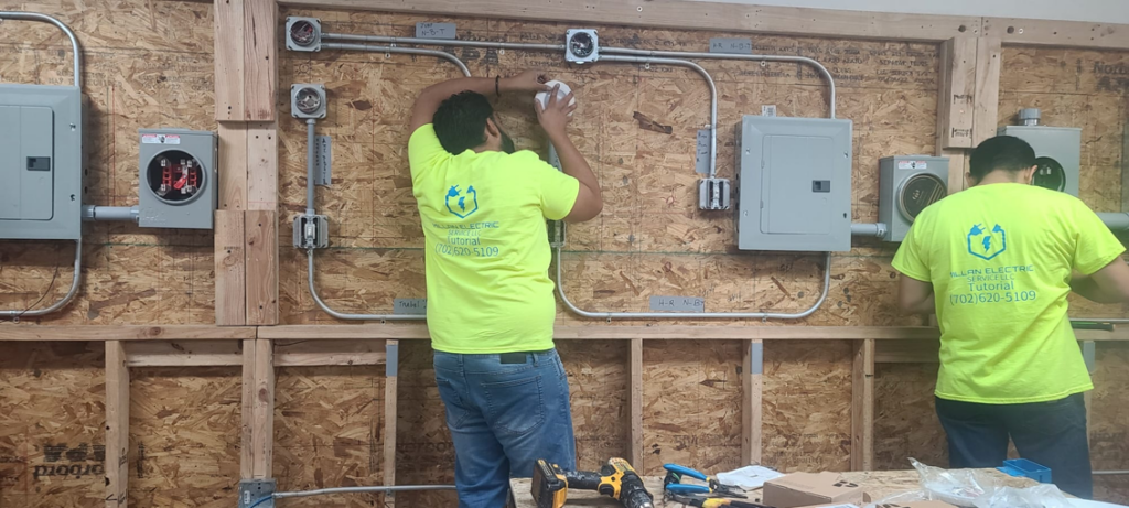 Two electricians installing electrical conduit and junction boxes on a wooden wall at Millan Electric Service llc in Las Vegas, NV