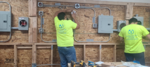 Two electricians installing electrical conduit and junction boxes on a wooden wall at Millan Electric Service llc in Las Vegas, NV
