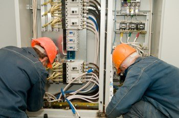 Two electricians in hard hats meticulously working on an open electrical panel, demonstrating expertise from Your Gilbert Electrician in Gilbert, AZ.