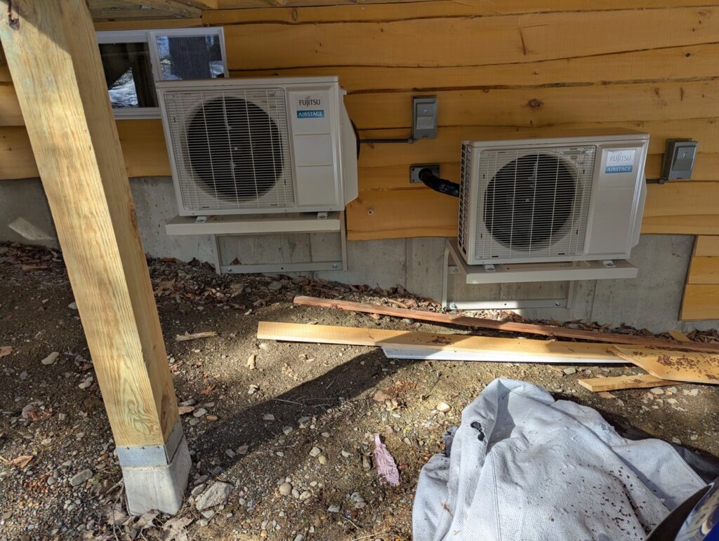 Two Fujitsu outdoor heat pump units installed on the side of a house by Kinney Family Heat Pumps in Augusta, ME.