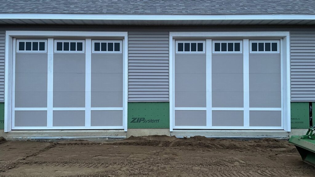 Two light grey garage doors with white trim installed on a new construction home by Superior Overhead Door, LLC in Granger, IN