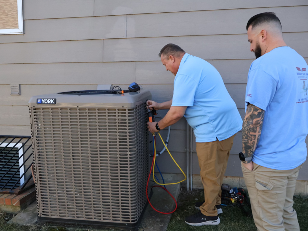 Two HVAC technicians servicing an outdoor York AC unit with gauges for Wright Way Air in Streamwood, IL