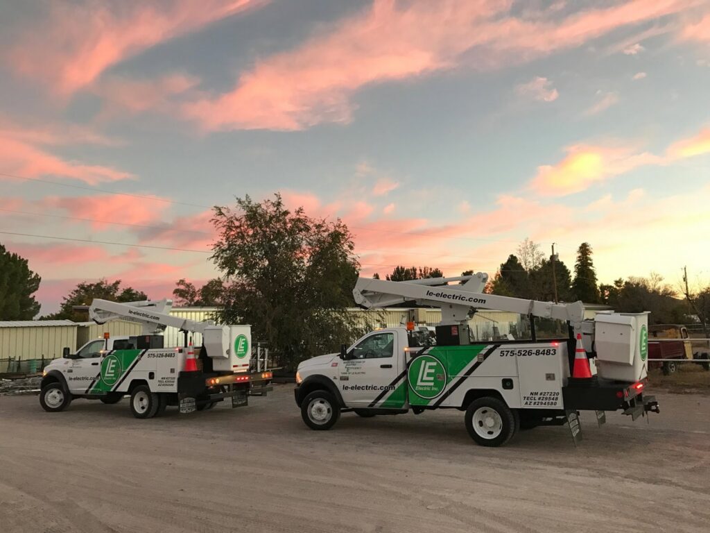 Two LE Electric service trucks with boom lifts parked at sunset, ready for electrical work in Las Cruces, NM