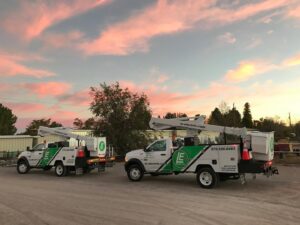 Two LE Electric service trucks with boom lifts parked at sunset, ready for electrical work in Las Cruces, NM