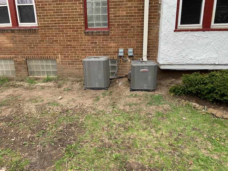 Two outdoor Lennox air conditioning units installed next to a brick house by Heating and Cooling Drs of Waukesha, Pewaukee, and Delafield, Waukesha, WI.