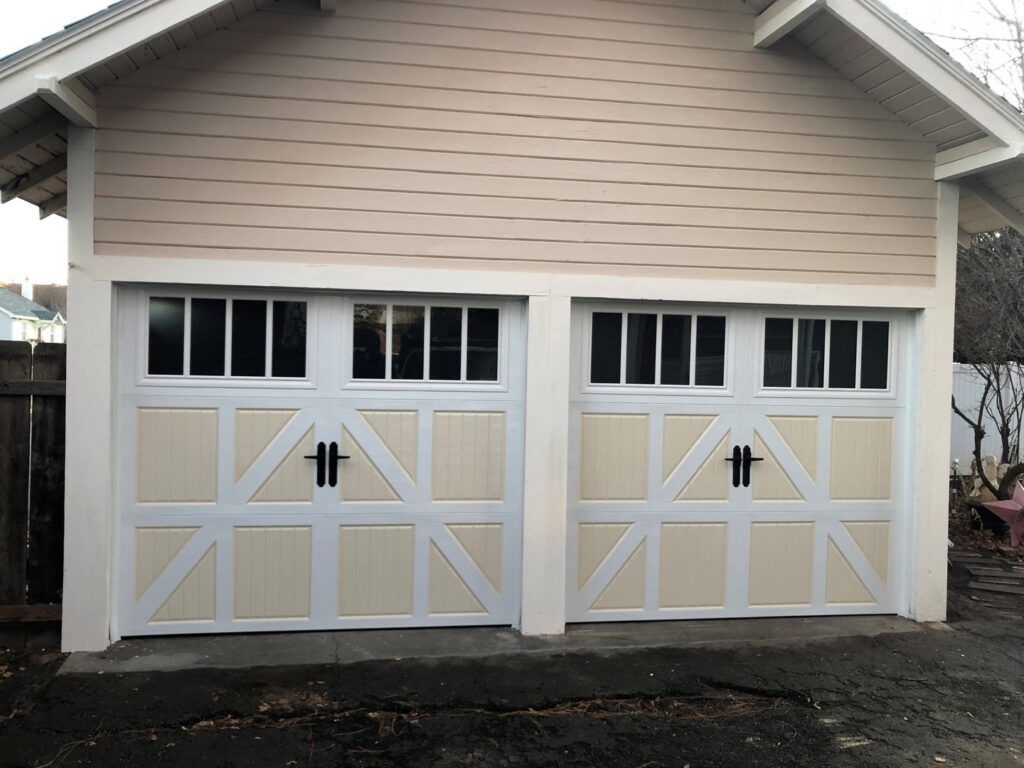 Two light-colored garage doors with decorative hardware and windows on a beige house by SCI Door in Yakima, WA