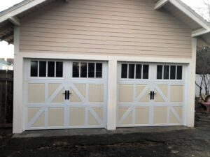 Two light-colored garage doors with decorative hardware and windows on a beige house by SCI Door in Yakima, WA