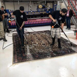 Two men pressure washing a large area rug as part of a cleaning service by the Association of Rug Care Specialists in Salem, OR