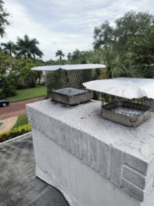 Two metal chimney caps installed on a white-painted brick chimney on a roof by A Sweep Across the Bay in Parrish, FL.
